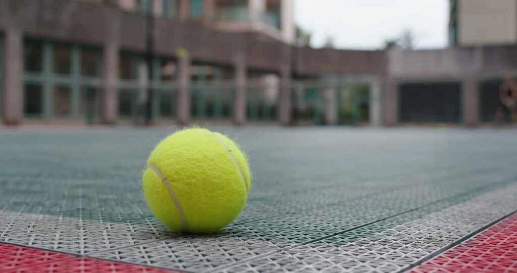 A tennis ball sits still on the edge of a court.