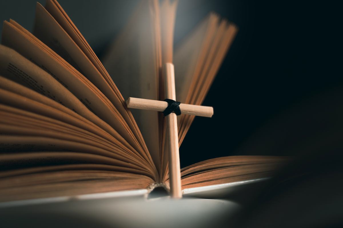 Open bible with cross standing upright against it.
